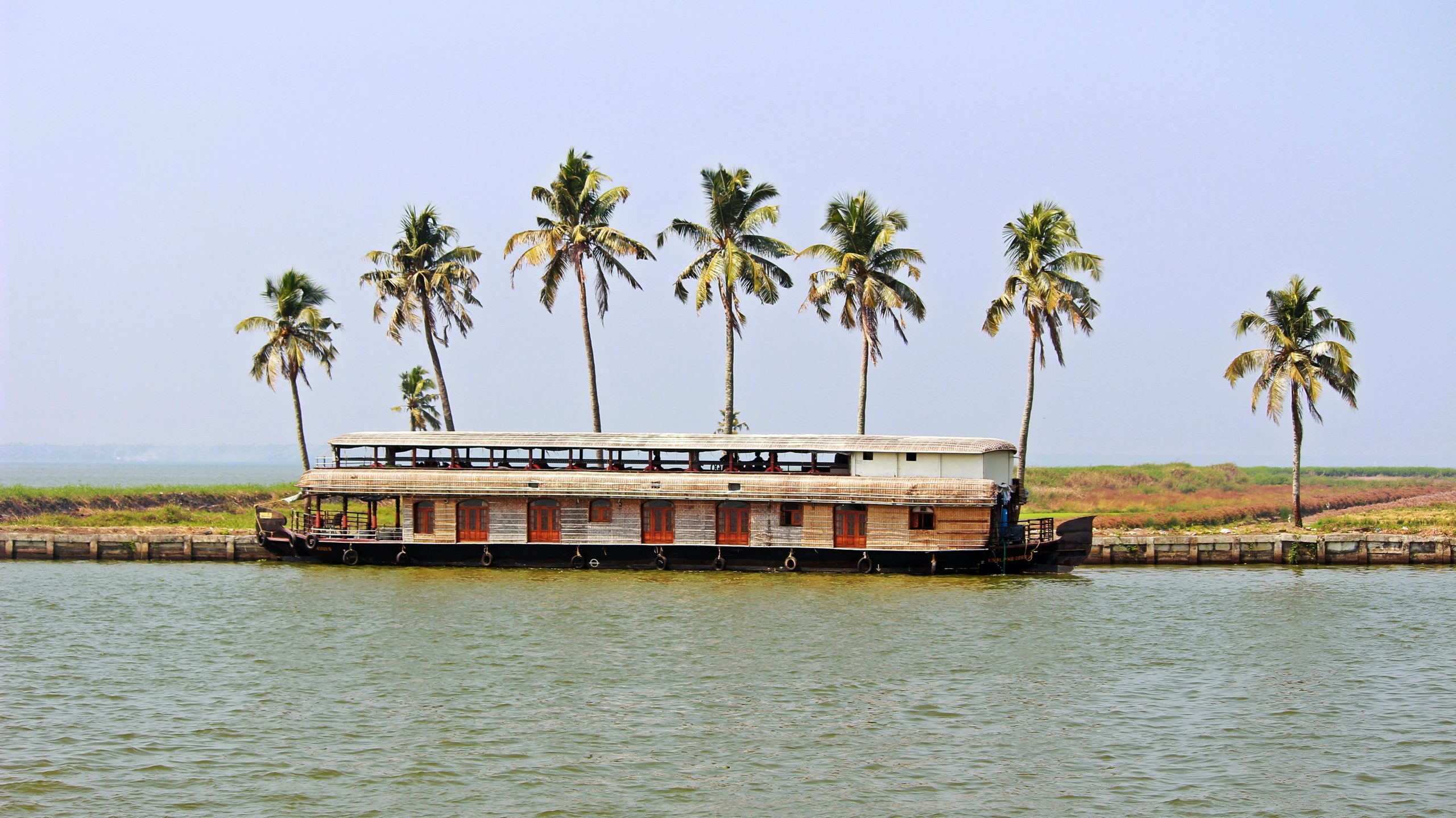 Scenic view of a houseboat and palm trees on the Kerala backwaters during daytime.
