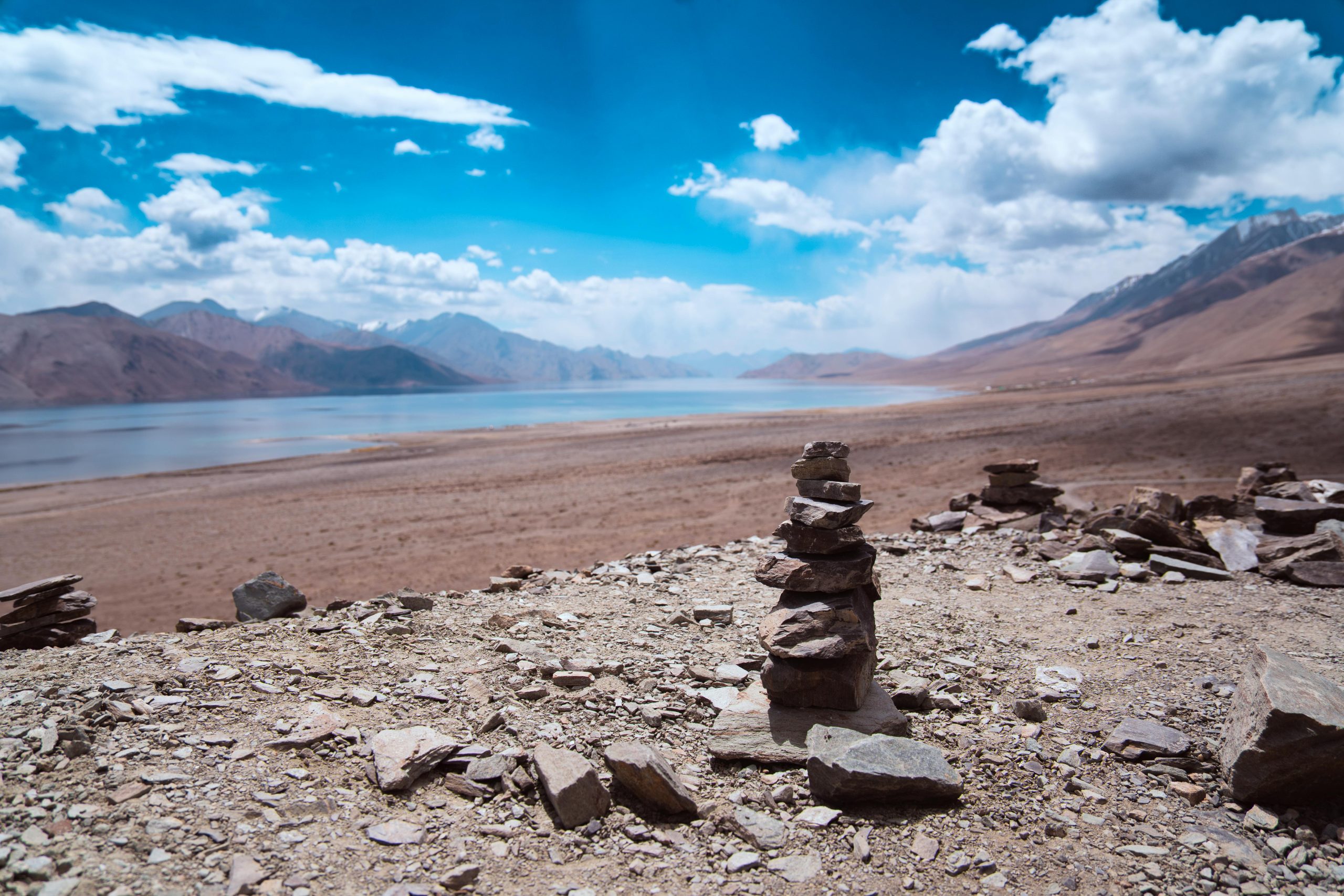 A stunning view of Pangong Tso Lake in Ladakh with rocky cairns in the foreground.